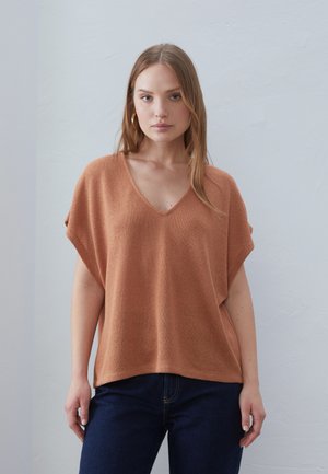 Top de punto color óxido con escote en V y mangas enrolladas, con un corte holgado y una tela texturizada. Combinado con vaqueros de denim azul oscuro.