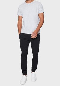 Szary t-shirt z krótkim rękawem w połączeniu z czarnymi dresami i białymi sneakersami; t-shirt jest prosty i z okrągłym dekoltem; dresy mają dopasowany krój.