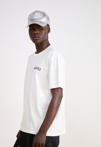 White cotton t-shirt with short sleeves and black "DICKIES" logo. Paired with a silver mesh cap featuring "Von Dutch" embroidered logo.