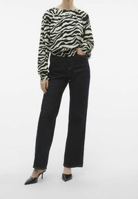 Blusa a maniche lunghe con stampa zebra bianco e nero, abbinata a pantaloni larghi in denim scuro a vita alta e mule con tacco alto neri.