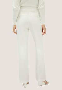 Pantaloni bianchi su misura con una forma svasata, dotati di tasche laterali e una texture liscia. Abbinati a un maglione chiaro con texture.