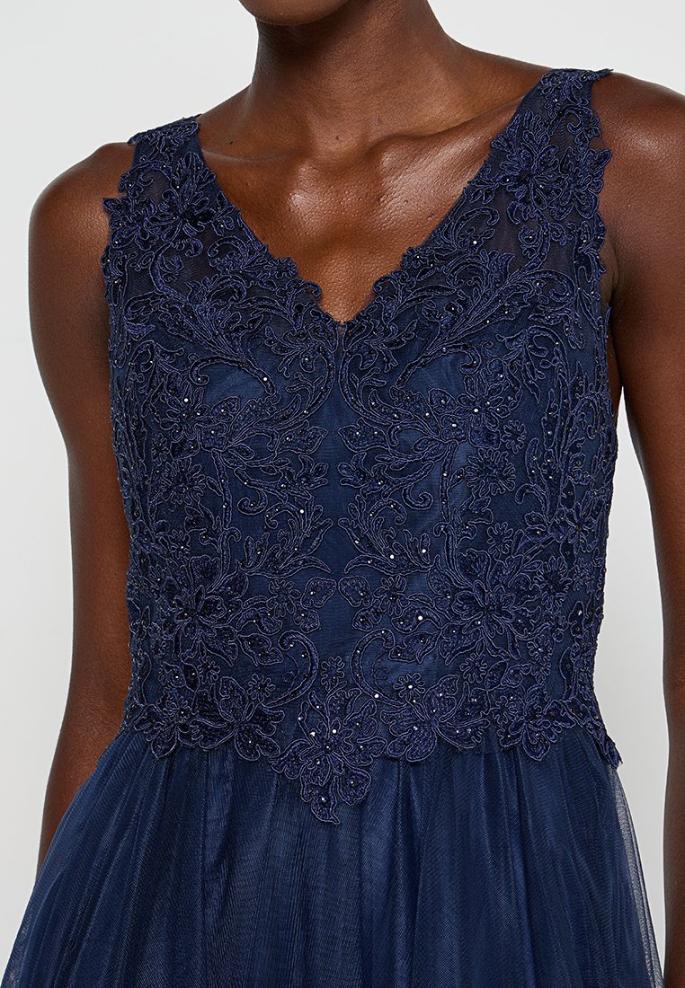 Granatowa suknia z dekoltem w kształcie litery V, ozdobiona misternym haftem kwiatowym i koralikami na górze, przezroczystą nakładką oraz tiulową spódnicą.