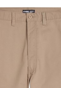 Pantalones chinos beige con una textura suave, que cuentan con un cierre de botón, trabillas para el cinturón y una etiqueta que dice "VANS AUTHENTIC CHINO" en el interior de la pretina.