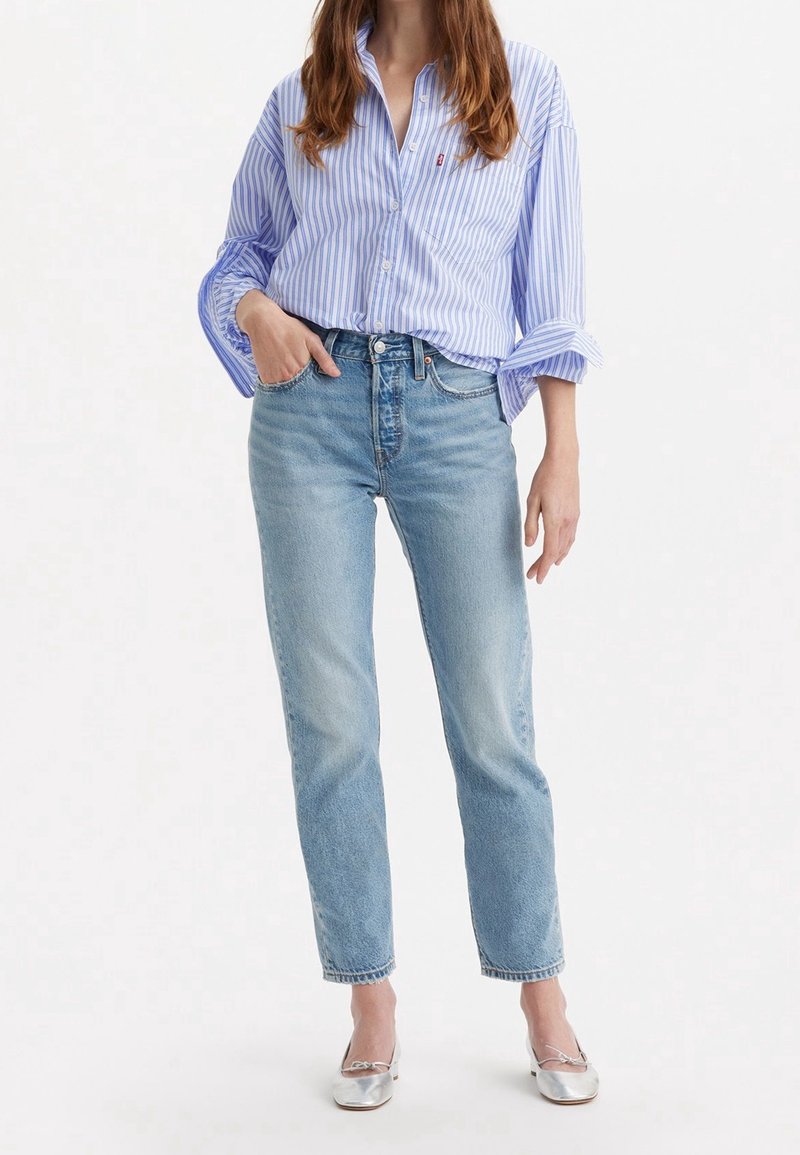 Ljusblå denimjeans med hög midja, rak benpassform och urtvättade detaljer. Matchas med en blå och vit randig skjorta med knappar. Silverfärgade ballerinaskor.