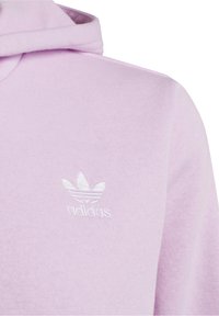 Lavendelkleurige hoodie met wit geborduurd Adidas trefoil-logo op de borst, waarbij een deel van de capuchon en schouder zichtbaar is.