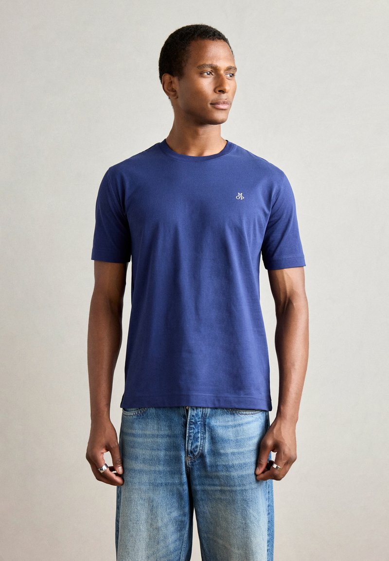 Marineblå bomulds T-shirt med korte ærmer, rund hals og et lille logo på venstre bryst. Kombineret med lyseblå denim jeans.