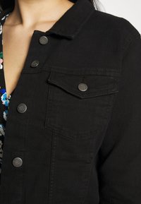 Czarna kurtka dżinsowa z klasycznym kołnierzem, z przodu zapinana na guziki oraz z kieszenią na piersi z metalowym zatrzaskiem. Gładka tekstura z minimalnymi detalami przeszyć.