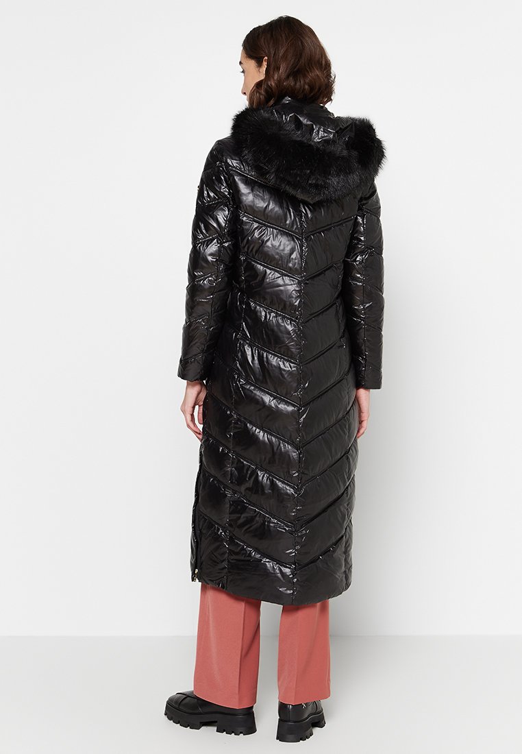 Cappotto pufffer nero con finitura lucida, dotato di cappuccio foderato in pelliccia e motivo a zig-zag. Design di lunghezza lunga con zip ai lati.