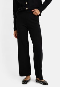 Pantalons large noirs en tissu doux, avec une ceinture élastique, associés à des ballerines noires décorées de clous en argent.