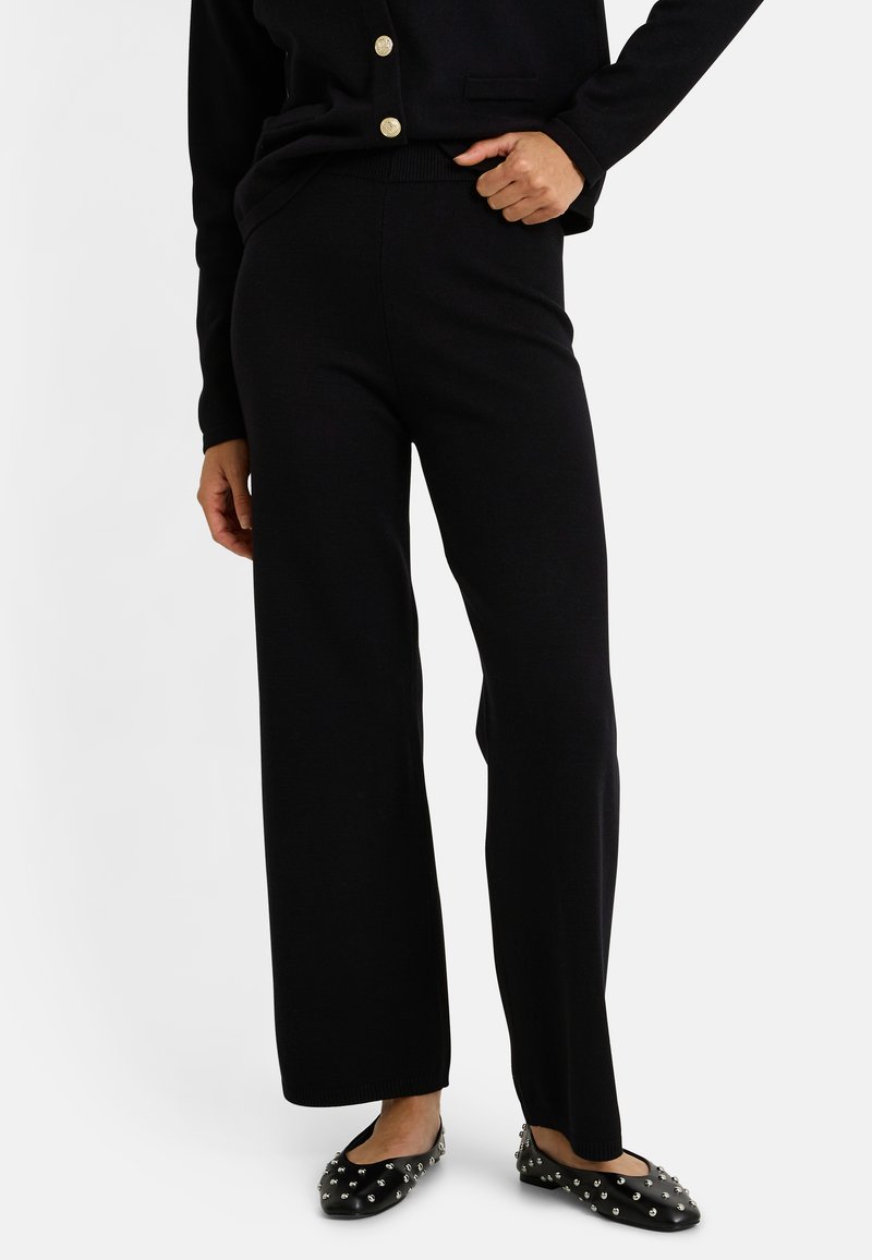 Pantalons large noirs en tissu doux, avec une ceinture élastique, associés à des ballerines noires décorées de clous en argent.