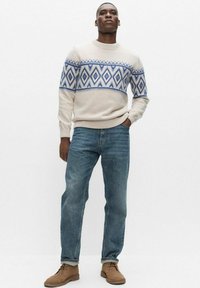 Beige neulepusero, jossa sininen timanttikuosi, yhdistetty vaaleansiniset farkut ja ruskeat kengät. Puserossa on ribbineulotut hihansuut ja helma.