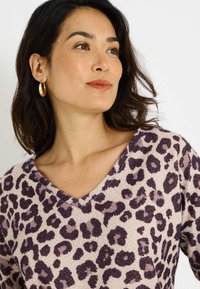 Jersey de pico en tela suave con una base de color beige claro y estampado de leopardo en púrpura. Presenta mangas 3/4 y un corte relajado, realzando la textura.