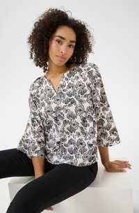 Blouse à imprimé floral en noir et blanc avec un décolleté en V et des manches trois-quarts. Tissu léger avec une texture lisse.