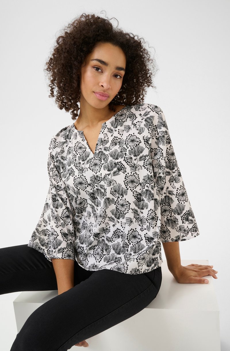 Blouse à imprimé floral en noir et blanc avec un décolleté en V et des manches trois-quarts. Tissu léger avec une texture lisse.