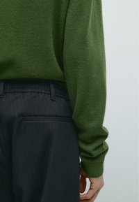 Maglione verde scuro a maglia con maniche lunghe, abbinato a pantaloni scuri a righe sottili, caratterizzati da una vestibilità comoda e una cintura elastica.