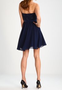 Marinblå midja-lös klänning med en åtsittande spetsöverdel och utsvängd chiffongkjol. Kombinerad med svarta klackar med en beige detalj på sulan.