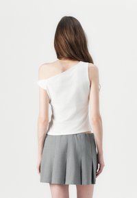 Top blanco de un solo hombro hecho de tela suave, con un cuerpo ajustado. Combinado con una falda corta plisada gris, que presenta una cintura elástica.