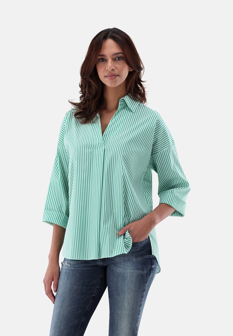 Green and white striped shirt with a collared neck, three-quarter sleeves, and a relaxed fit. Worn with blue jeans, features a pocket.