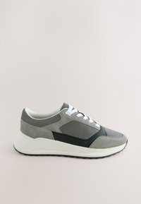 Grå og sort afslappet sneaker med hvid sål og snørebånd, mesh- og ruskindsoverdel, sideudsigt på en ensfarvet lys baggrund.