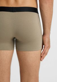 Beige Shorts aus weichem Stoff mit schwarzem elastischem Bund und enger Passform, mit sichtbaren Nahtdetails an den Nähten.