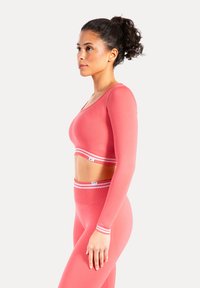 Top corto rosa a maniche lunghe con scollo a U e banda a strisce bianche. Leggings a vita alta abbinati con dettagli a strisce simili.