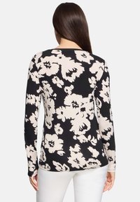 Długi rękaw bluzki w czarno-kremowy kwiatowy wzór. Miękka tkanina z okrągłym dekoltem i dopasowanym krojem, z zaokrąglonym dołem.