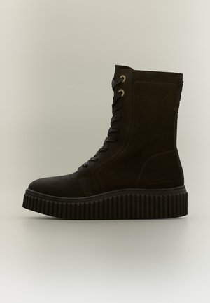 Botte haute en daim noir à lacets, semelle épaisse rainurée et œillets métalliques, vue de profil sur un fond neutre.