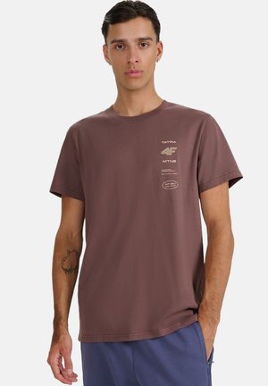Brązowa koszulka z krótkim rękawem wykonana z bawełny, z okrągłym dekoltem, nadrukowanymi jasnymi logo na przodzie oraz luźnym krojem.