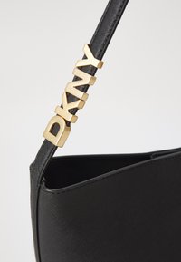Black handbag with a structured design, featuring a textured surface. Gold metal lettering "DKNY" accents the strap.