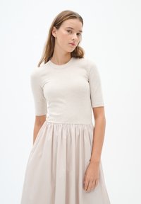 Beige gerippter Strickoberteil mit kurzen Ärmeln, kombiniert mit einem plissierten, hellrosa Rock, der ein eng anliegendes Oberteil und fließenden Stoff hat.