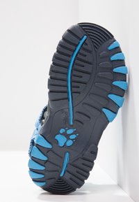 Modrý a černý podrážka sportovní obuvi s texturovanou gumou pro lepší přilnavost, hlubokými drážkami a modrým logem ve tvaru tlapky.
