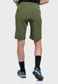 Olivgrüne Shorts mit geradem Schnitt, versehen mit einer glatten Textur und einer Gesäßtasche. Tragen Sie sie mit schwarzen Socken und Sportschuhen mit blauen Akzenten.