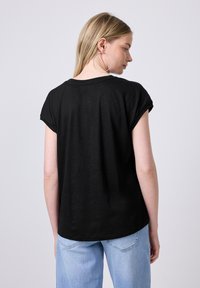 Černé tričko s krátkým rukávem a volným střihem, s oblečenými světle modrými džíny s vysokým pasem. Modelka má dlouhé, rovné vlasy.
