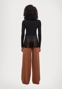 Cămășă neagră cu mânecă lungă, având detalii cu franjuri la spate, asortată cu pantaloni cu talie înaltă și cu picioare largi de culoare maronie. Textură de țesătură netedă.