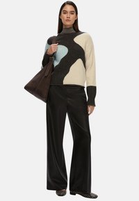 Maglione lavorato a maglia con motivi astratti in grigio, azzurro chiaro e crema; abbinato a pantaloni neri a gamba larga e una borsa in pelle marrone scuro.