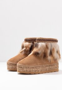 Ett par bruna mocka ankellängd stövlar med vävda plattformssulor och flerfärgad fuskpäls runt de övre kanterna.