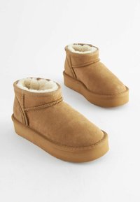 Brune ruskind ankelstøvler med blød faux fur-fór, rund tå og flade gummisåler. Inkluderer enkel stropdetalje på siden.