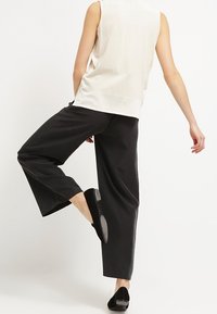 Svarta vida byxor i mjukt material, i kombination med en ljusbeige ärmlös topp. Har en bekväm passform och minimal detaljering.