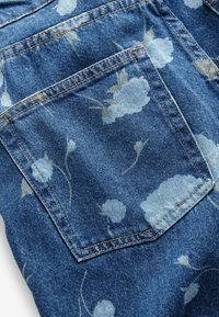Tela de mezclilla con un estampado floral azul, que cuenta con un bolsillo trasero. Costuras en contraste y una superficie texturizada completan el diseño.