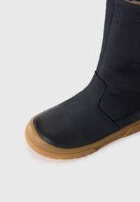 Navy blauwe enkellaars van textuurleer met een ronde neus, tan rubberen zool en contrasterende stiksels.