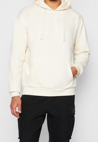 Krémová mikina s kapucí vyrobená z bavlněné směsi, má přední kapsu, kapuci se stahovací šňůrkou a decentně vyšívané logo. Dlouhé rukávy s elastickými manžetami.