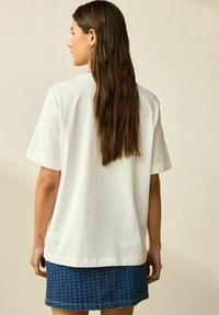 Weißes Baumwoll-T-Shirt mit lockerem Schnitt, kurzen Ärmeln und geradem Saum, kombiniert mit einem blauen karierter Jeansrock.