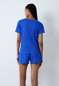 Set da lounge blu composto da una maglietta a maniche corte e pantaloni shorts. Il tessuto è morbido con una finitura leggermente strutturata. Vestibilità comoda e design atletico.