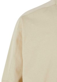 Beige rövid ujjú póló, amely kerek nyakkivágással, sima pamut anyagból készült, és diszkrét varrási részletekkel rendelkezik a vállvarrások mentén.