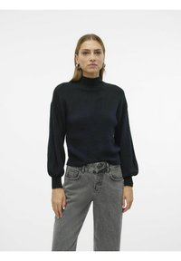 Svart stickad tröja med hög halsringning och puffärmar, tillsammans med högmidjade grå jeans med sidofickor och en strukturerad yta.