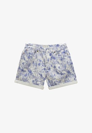 Close-up af blåt og hvidt mønstret stof med detaljerede bygninger og palmer, med et hvidt læderetiket prydet med "Joules."