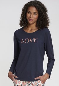 Navy long-sleeve shirt with round neckline featuring "LOVE yourself" text in pink and white. Soft fabric, relaxed fit. Patterned pants visible.