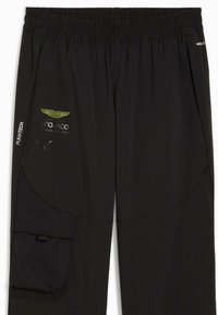 Schwarze Hose aus leichtem Stoff, mit elastischem Bund, Seitentasche und Logo-Akzenten in Grün und Weiß.