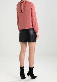 Blusa rosa a maniche lunghe con un nodo dietro, abbinata a una mini gonna nera in pelle. Stivali alla caviglia neri completano l'outfit.