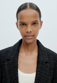 Schwarzer strukturiert blazer über einem weißen gerippten Oberteil. Der Kragen ist mit einem Ausschnitt versehen und der Blazer hat eine strukturierte Passform, die das Dekolleté betont.